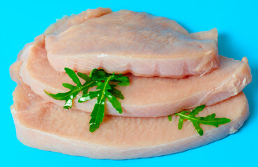 fresh turkey steaks with pepper and arugula on blue background