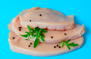 fresh turkey steaks with pepper and arugula on blue background