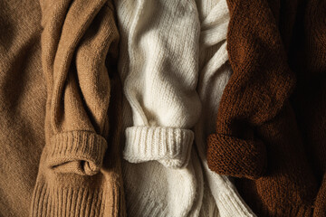 Three colorful warm woolen winter sweaters / pullovers. Beige, white, brown. Minimalistic fashion...