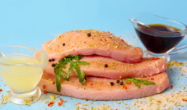 fresh turkey steaks with pepper and arugula on blue background, soy sauce and lemon juice for marinade