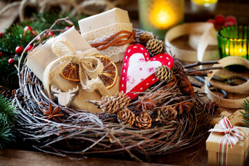 Eco friendry zero waste gift wrapping concept. Beautiful xmas presents in brown kraft paper decorated with dried oranges, pine cones and burlap ribbon with lit candles at the background