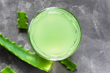 Aloe Vera juice and green aloe leaves on a gray background. Top view