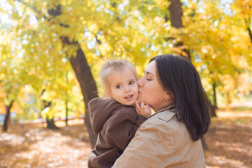 A young mother and little daughter are walking and laughing in the autumn park. Family. Autumn mood