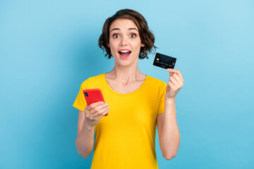 Photo of lovely amazed lady hold telephone credit card open mouth wear yellow t-shirt isolated blue color background