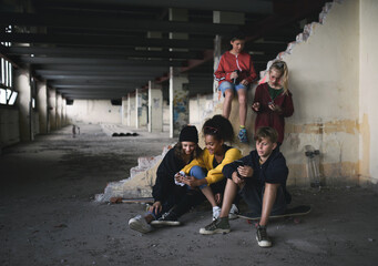 Fototapeta na wymiar Group of teenagers gang sitting indoors in abandoned building, using smartphones.