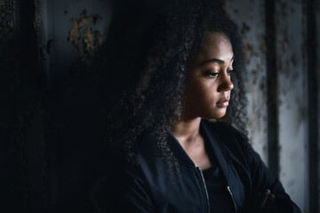 Portrait of sad mixed-race teenager girl standing indoors in abandoned building.