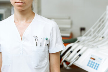 Young female doctor stands in the dental office. Chest pocket contains tools and a toothbrush....