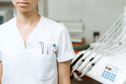 Young female doctor stands in the dental office. Chest pocket contains tools and a toothbrush. Concept of attending dentist, dental care and going to the dental clinic