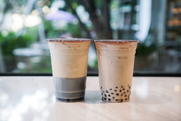Iced bubble milk tea and milk with grass jelly. Two plastic cup of drinks, fresh milk with grass jelly and milk tea with boba/bubble tapioca pearls.