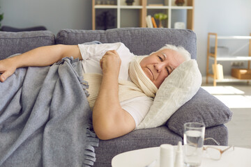 Unhappy senior man lying on sofa at home, suffering from bad cold, flu or covid fever
