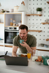 Fototapeta na wymiar Young man eating breakfast and reading the news online. Handsome man enjoying at home.