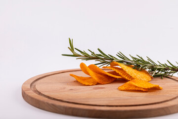 Potato chips with a sprig of rosemary in a glass bowl on a wooden table.