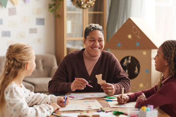 Fototapeta premium Portrait of smiling African-American woman teaching art class with kids enjoying drawing in school