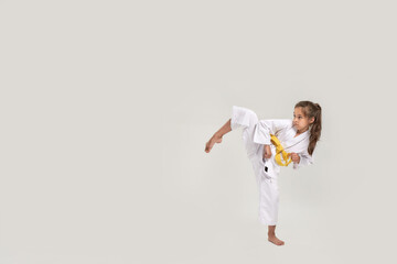 Full length shot of little karate girl in white kimono with a yellow sash exercising and fighting, doing martial arts, standing isolated over white background © Svitlana