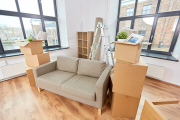 repair, moving and real estate concept - sofa and corrugated boxes with stuff at new home