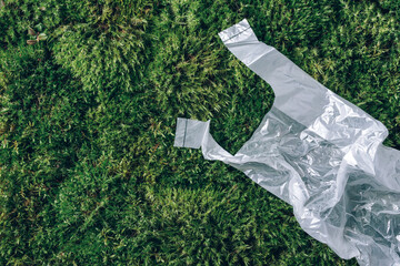 Disposable plastic bag on green moss, grass background. Pollution problem concept. Top view. Copy space. Environmental pollution problem. Garbage, waste collection and sorting, trash outdoors