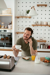 Fototapeta na wymiar Young man drinking coffee and talking to the phone. Man preparing sandwich