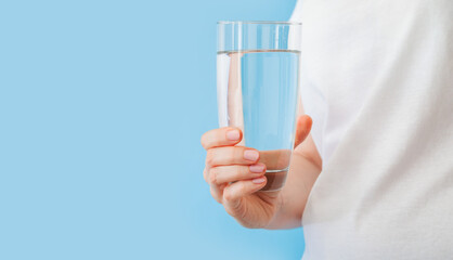 Woman holding glass with water in hand on color blue background with copy space. Healthy lifestyle and fitness concept.