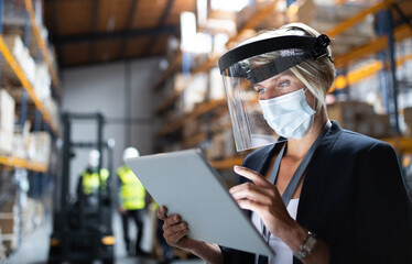 Manager with protective shield using tablet indoors in warehouse, coronavirus concept.