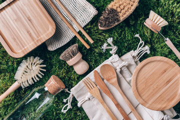 Zero waste concept. Cotton bag, bamboo cutlery, glass jar, bamboo kitchen brushes, straws on green moss background. Top view. Copy space. Sustainable zero waste kitchenware utensils and eco dishware