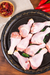 Raw chicken drumsticks on black frying tray with ingredients and spices, top view