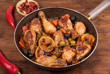 Ready Algerian chicken with vegetables and olives with spicy sauce in a pan on the table with hot peppers, top view
