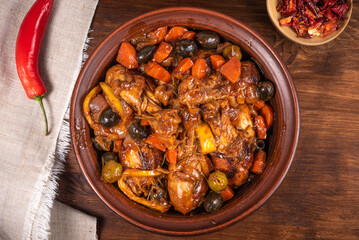 Ready chicken on Algerian tagine with olives and vegetables with spicy sauce on a wooden table, top...