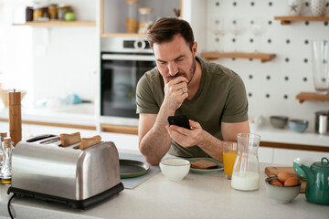 Young man eating breakfast and reading the news online. Handsome man enjoying at home.