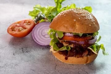 Burger, hamburger, cheeseburger, in bun with lettuce, tomato, onion, bacon, delicious fast food, on cement floor background.