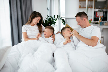 Fototapeta premium Young family enjoying in bed. Happy parents with sons relaxing in bed...