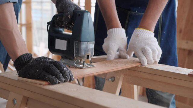 Close up of experienced carpenter in working on wood craft saw and processes the edges of a wooden bar with a jig saw in workshop. Slow motion.
