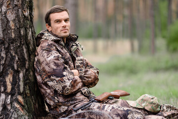 Lonely Hunter in Camo Has Rest Sitting under Tree.