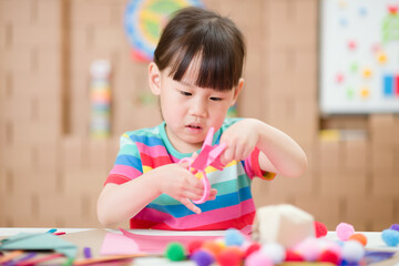 young girl using scissors cutting papper for making craft for homeschooling