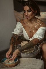 Portrait of a young beautiful lady modeling a pot of clay with her hands. Spots of clay on her body
