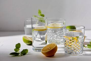 drink, detox and diet concept - glasses with fruit water or lemonade, lemons, limes and peppermint...