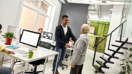 Fototapeta premium Aged man, senior intern and young guy shaking hands, Young team greeting new worker in the modern office