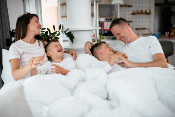 Young family enjoying in bed. Happy parents with sons relaxing in bed...