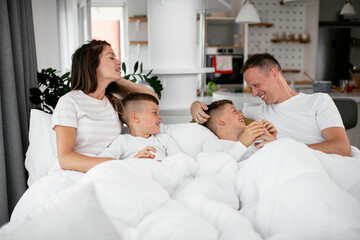Obraz na płótnie Canvas Young family enjoying in bed. Happy parents with sons relaxing in bed...