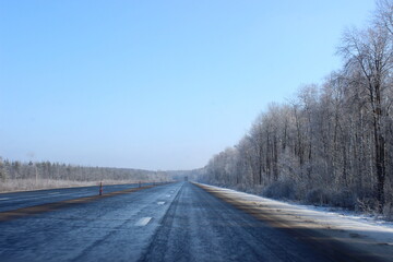 Beautiful European suburban empty endless black wet asphalt winter road landscape with white snow covered frosty trees on roadside in perspective at cold Sunny winter day on clear blue sky background