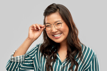 people, education and school concept - portrait of happy asian woman in glasses or student over grey background