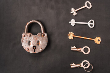 Closed old rusty lock and many keys lying around on black background. Looking for problem solution concept