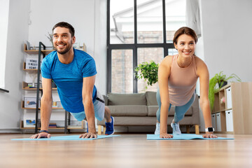 sport, fitness, lifestyle and people concept - smiling man and woman exercising and doing plank at home