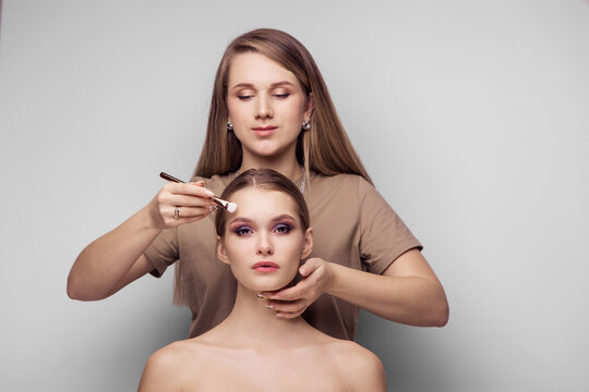 Make-up artist makes a demonstration make-up on the model. Master Class. Profession visagist young woman. Gray background place for text. Beauty salon. Fashion