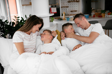 Obraz premium Young family enjoying in bed. Happy parents with sons relaxing in bed...