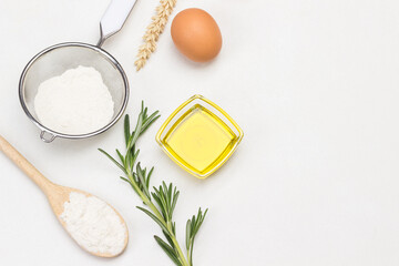 Flour in wooden spoon, sieve and glass jar. Olive oil and sprig of rosemary.