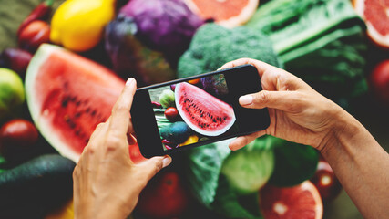 Table with delicious meals and plates. Fruits and vegetables. Woman's hands with mobile phone taking food photo