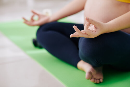 Close-up image of pregnant woman sitting in lotus position, making mudra hand gesture and meditating