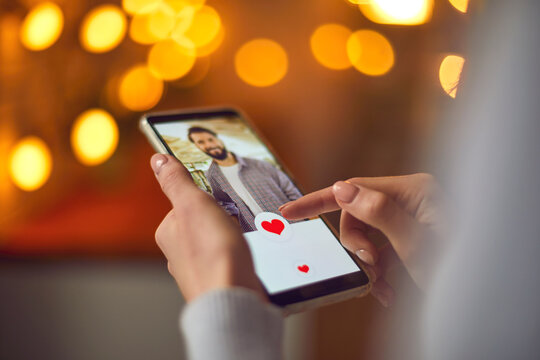 Closeup of woman looking at young man's profile photo on dating app and pressing like button