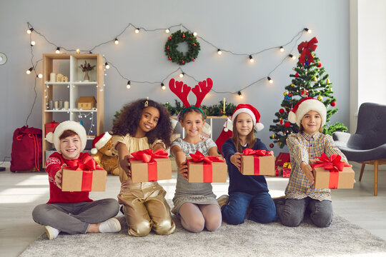 Children of different nationalities sit in a row and hold out Christmas presents in front of them.