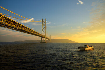 夕日に輝く明石海峡大橋と小舟